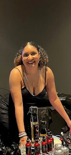 Picture of Chimira smiling and leaning over a table of herbs and oils products working a pop-up shop.