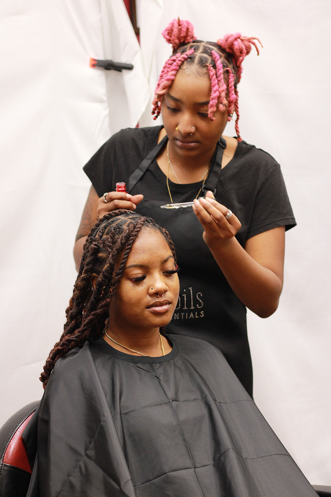 Stylist applying Herbs and Oils, Last Call Finishing Oil to scalp after client has gotten a braided style with hair added to ensure the health of the scalp and edges during a protective style.