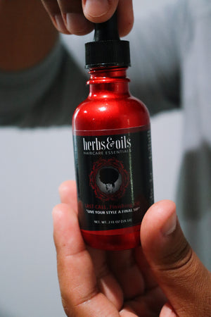 Red bottle with black cap held by a person against a neutral background.  hair finishing oil, lightweight hair oil natural, oil for thinning edges, hair growth oil natural, oil for dry hair ends, sealing oil for natural hair, scalp oil for hair growth, beard oil natural, oil for moisture retention hair