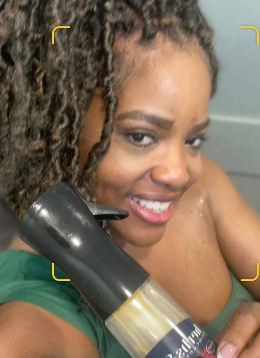 Close up picture of Reina Short with a faux loc style holding a bottle of Herbs and Oils Hair Tonic