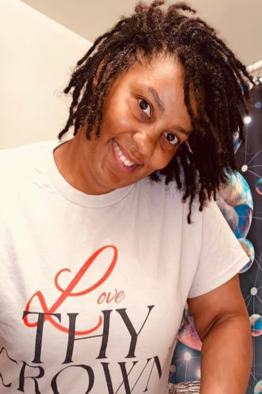 Lady with slightly salt and pepper, shoulder length locs wearing an herbs and oils tee shirt